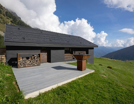 A very unusual Swiss mountain chalet because it is black and made of wood. Surrounded by a beautiful green summer meadow. The sky is blue and it looks like a quiet and very peaceful place. A very modern grill for cooking meat outside.の写真素材