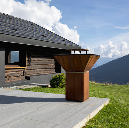 A very unusual Swiss mountain chalet because it is black and made of wood. Surrounded by a beautiful green summer meadow. The sky is blue and it looks like a quiet and very peaceful place. A very modern grill for cooking meat outside.の写真素材