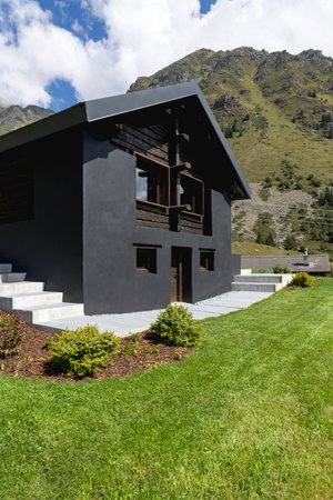 A very unusual Swiss mountain chalet because it is black and made of wood. Surrounded by a beautiful green summer meadow. The sky is blue and it looks like a quiet and very peaceful place.の写真素材