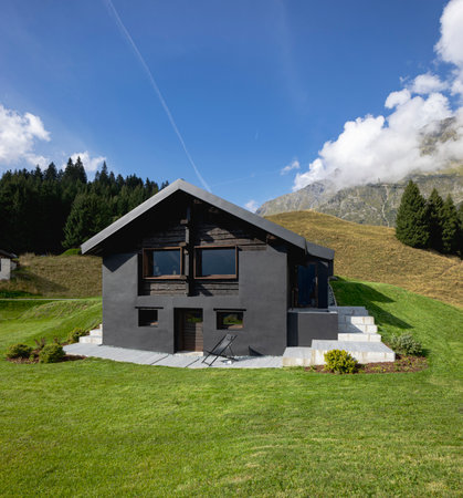 A very unusual Swiss mountain chalet because it is black and made of wood. Surrounded by a beautiful green summer meadow. The sky is blue and it looks like a quiet and very peaceful place.の写真素材