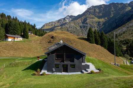 A very unusual Swiss mountain chalet because it is black and made of wood. Surrounded by a beautiful green summer meadow. The sky is blue and it looks like a quiet and very peaceful place.の写真素材