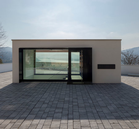 A stylized entrance to a residential building where the entrance is above and then you have to go down to access the flats. On the other side of the entrance you can see a lake through the glass panes.の写真素材