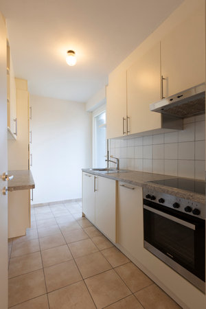 Old white kitchen with an oven, sink and cabinets. Light on and no one insideの写真素材