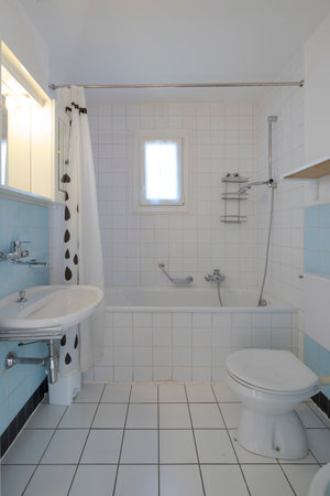 Old bathroom with white tiles, at the end there is a bathtub with shower and open curtain. There is also a small window. Nobody insideの写真素材