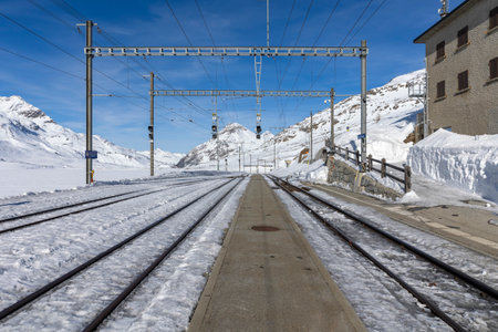 Train station on the Bernina Pass in Switzerland. Front view from the railway platform and tracks appearing from the snow. Nobody insideの写真素材