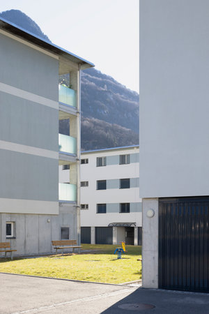 Detail of a residential complex with garden and games for children. There is blue sky and mountains behind, no one insideの写真素材
