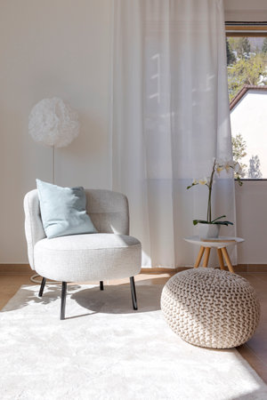 Detail of a living room corner with a small armchair with a coffee table and a pouf resting on the carpet. No one insideの写真素材