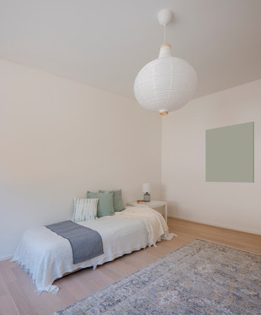 Detail of a single bedroom with a bed covered with blankets and many pillows. There is a nice carpet on the floor and space for a painting on the side. No one inside.の写真素材