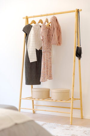 Detail of a wooden rella with elegant women's clothes hanging from it. In the foreground you can see part of the bed with blankets. No one insideの写真素材