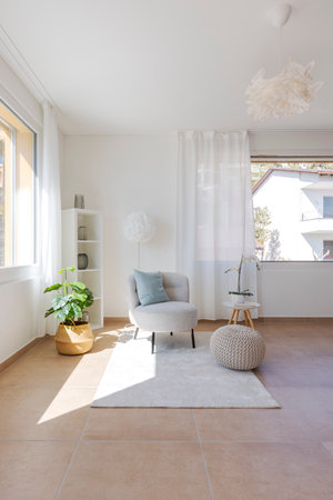 Detail of a living room corner with a small armchair with a coffee table and a pouf resting on the carpet. No one insideの写真素材