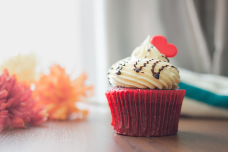 Red cupcakes with cream on top and heart-shaped sugar placed on the table near the window in the morning, vintage tone.の写真素材