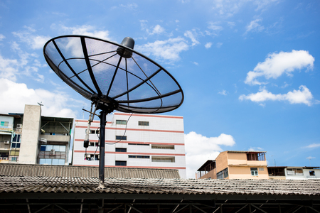 A satellite dish on the roof with a building and sky background.の写真素材