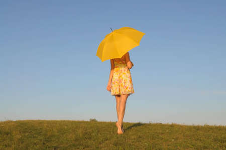The harmonous woman in a yellow dress with an umbrella stands on a lawn against the skyの写真素材