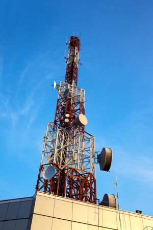 Red and white antenna (cellular tower) under blue sky.の写真素材
