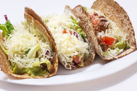 3 tacos. Mexican food created with tortillas, cream cheese, cooked chopped meat, avocado sauce, lettuce, and tomato salad, with cheese on top. perspective lookの写真素材