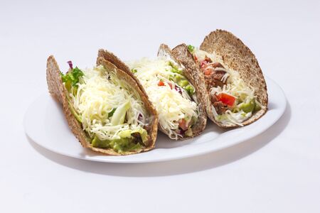 3 tacos. Mexican food created with tortillas, cream cheese, cooked chopped meat, avocado sauce, lettuce, and tomato salad, with cheese on top. white backgroundの写真素材