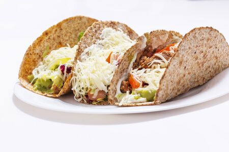3 tacos. Mexican food created with tortillas, cream cheese, cooked chopped meat, avocado sauce, lettuce, and tomato salad, with cheese on top.の写真素材