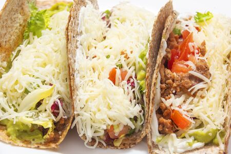 3 tacos. Mexican food created with tortillas, cream cheese, cooked chopped meat, avocado sauce, lettuce, and tomato salad, with cheese on top. Close up lookの写真素材