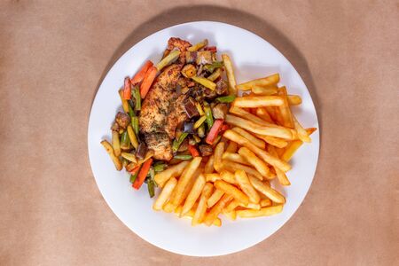 A nice plate of roasted chicken, seasoned with herbs, pepper, salt, oregano, and garlic. Also accompanied by vegetables fried on olive oil. Accompanied by French fries on a white plate.の写真素材