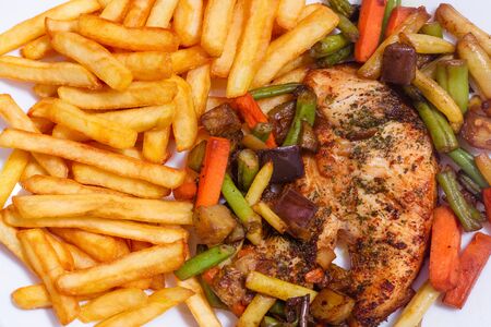 A nice plate of roasted chicken, seasoned with herbs, pepper, salt, oregano, and garlic. Also accompanied by vegetables fried on olive oil. Accompanied by French fries on a white plate.の写真素材