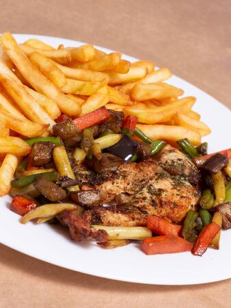 A nice plate of roasted chicken, seasoned with herbs, pepper, salt, oregano, and garlic. Also accompanied by vegetables fried on olive oil. Accompanied by French fries on a white plate.の写真素材