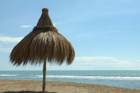 straw umbrella parasol on the beach with calm open expanse of sea and skyの写真素材