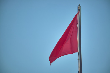 Pole with raised red flag, symbol of danger for bathers and navigators.の写真素材