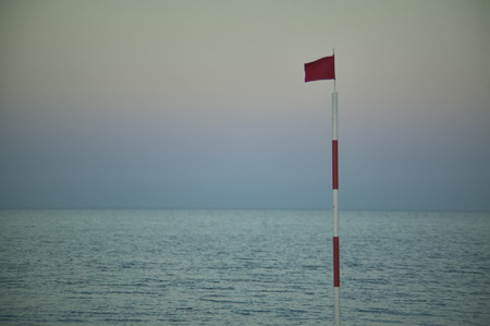 Pole with raised red flag, symbol of danger for bathers and navigators.の写真素材