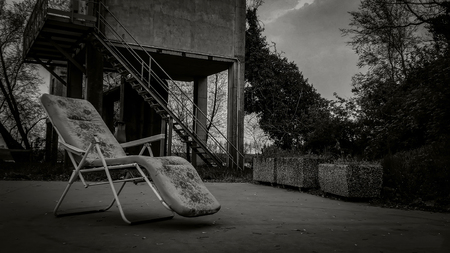 Composition with an old deck chair in an abandoned place with a very dull and gloomy appearance: a horror movie scenario.の写真素材