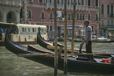 Gondolier waiting for his next race over his gondola, moored at a pier.のeditorial素材