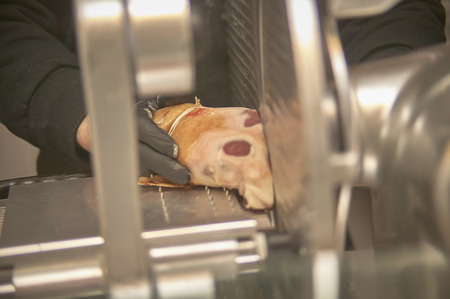 Hands of an operator at the supermarket slicing a piece of ham on an electric electrician.の写真素材