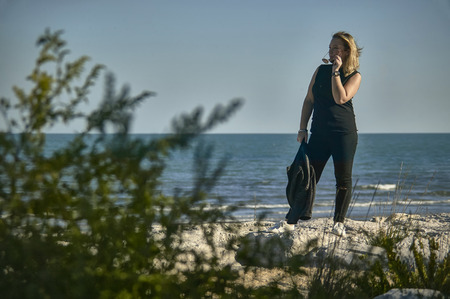 Full-length portrait set in the beach of a blonde girl who garda on the left while preparing to wear sunglasses.の写真素材