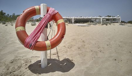 Symbolic image of a life buoy with rope hanging on a pole in the beach.の写真素材