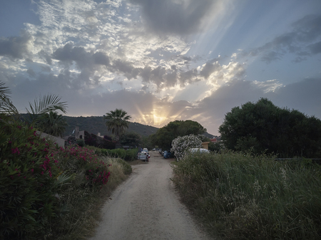 Sardinia's hilly landscape of sun lit by the sunset with the sun going to disappear behind the clouds letting glimpse of its shining rays.の写真素材
