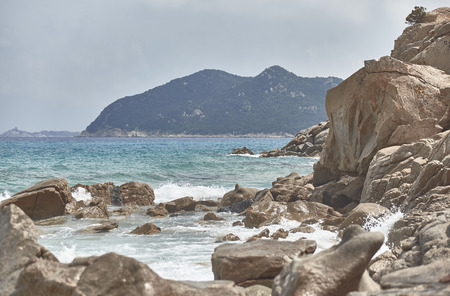 Mountain on the sea in the south of Sardinia filtered by a cliff during the summer with sea waves crashing on the rocks.の写真素材
