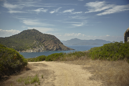 Small dirt road that leads down from the mountain in a beach created on a natural bay in the south of Sardinia.の写真素材