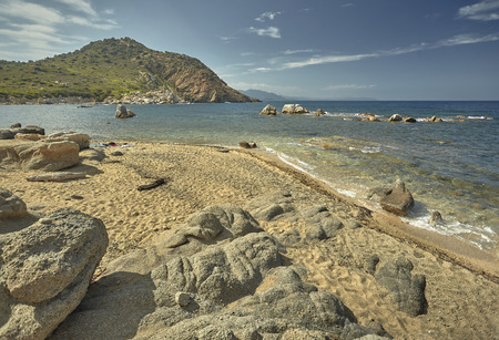 Beautiful seascape of the Cala Sa Figu beach in the south of Sardinia, with the rocks in the foreground, the beach and the curly mountains of vegetation in the background during the summer.の写真素材