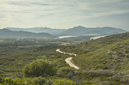 Hilly landscape typical of the coast of southern Sardinia with a dirt road leading downstream towards the sea.の写真素材