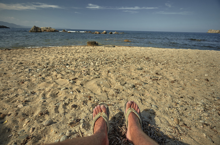 Mediterranean beach with the background sea and the feet of a person in the foreground: symbol of vacation, relaxation and solitude in the middle of nature.の写真素材