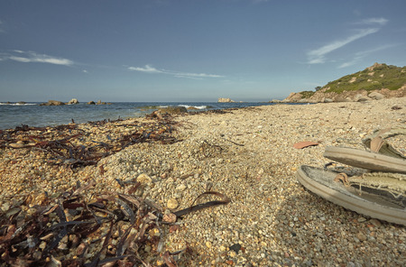 Detail of a Mediterranean beach during the summer with a pair of flip-flops sprouting on the right side of the image.の写真素材