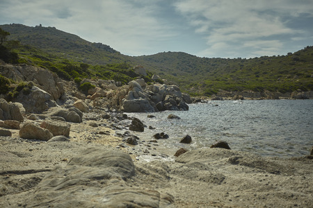 Jagged rocks with some green hills that merge into the Mediterranean sea.の写真素材