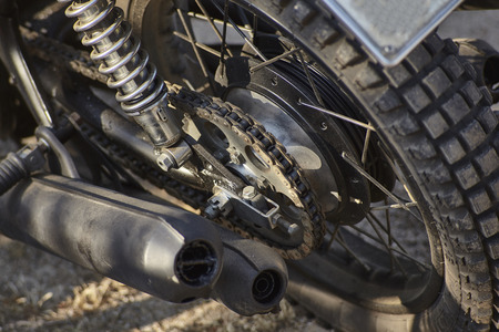 Detail of the chain transmission on the crown of an old vintage motorcycle with the mufflers on the side, the drum brake and the spoked wheel supported by the shock absorber.の写真素材
