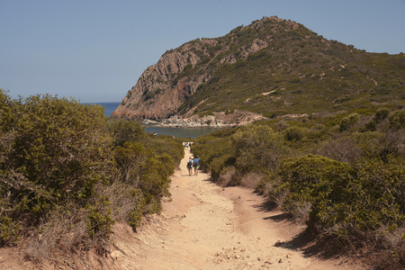 Hikers walking in a dirt road in the middle of the hills on the south coast of Sardinia in Italy as they head for the sea.の写真素材