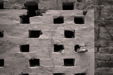 Detail of an old historical building with a portion of wall with holes and a geographic map attached and a shoe tucked into one of the holes.の写真素材