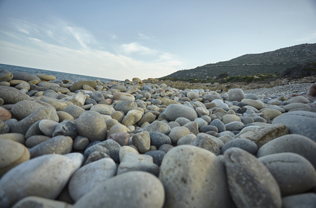 Detail of some white pebbles on a typical beach of the southern coast of southern Sardinia in Italy, with the background of the rest of the beach and the sea.の写真素材