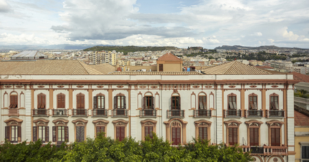 Side detail of a historic building in the city center of Cagliari in Italy, with behind the city panorama under a sky full of clouds.の写真素材