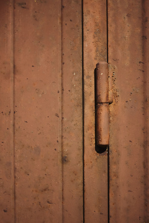 Detail of the hinge of a brown metal door, rusted and ruined by weather and bad weather. Vertical shot.の写真素材