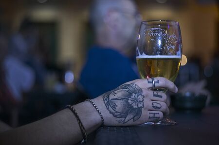 Tattooed hand holds glass of beer at nightの写真素材