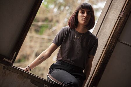 Brunette girl sitted on a window of an old and abandoned houseの写真素材