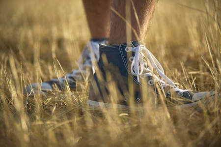 Shoe in the foreground with behind the other while being worn by a boy walking in the grass.の写真素材